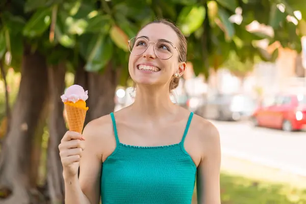 Young pretty woman with a cornet ice cream at outdoors looking up while smiling