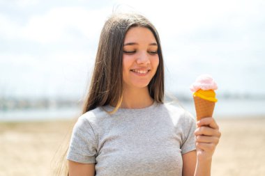 Açık havada kornet dondurmalı genç bir kız, neşeli bir ifadeyle.