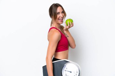 Beyaz arka planda, tartı makinesi ve elmasıyla izole edilmiş genç beyaz bir kadın.