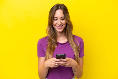 Sarı arka planda izole edilmiş genç beyaz kadın cep telefonuyla mesaj ya da e-posta gönderiyor.