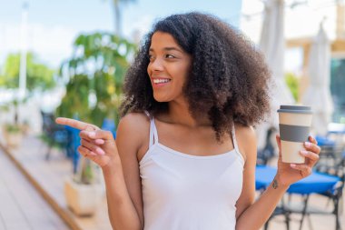 Genç Afro-Amerikalı bir kadın açık havada kahvesini yudumlarken yan tarafı göstererek bir ürün sunuyor.