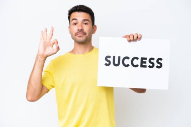 İzole edilmiş beyaz arka planda genç yakışıklı bir adam. Elinde bir levha var. SUCCESS ve zaferi kutluyor.