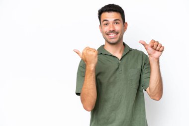 Soyutlanmış beyaz arka planda genç yakışıklı bir adam bir ürün sunmak için kenarı işaret ediyor.