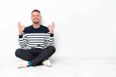 Young man sitting on the floor isolated on white background in zen pose