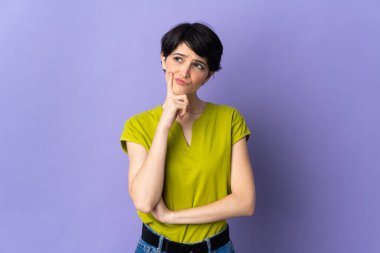 Kısa saçlı bir kadın mor arka planda izole edilmiş, yukarı bakarken şüpheleri var.