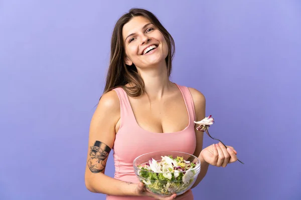 Young slovak woman isolated on purple background holding a bowl of salad with happy expression