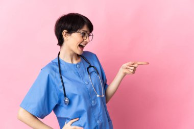 Pembe arka planda izole edilmiş bir cerrah parmağını yana uzatıyor ve bir ürün sunuyor.