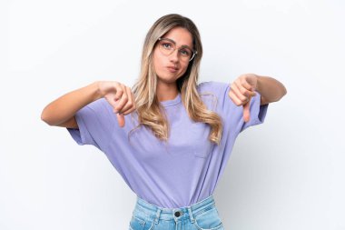 Genç Uruguaylı kadın beyaz arka planda izole edilmiş, baş parmağını iki eliyle aşağı gösteriyor.