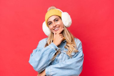 Genç, güzel Uruguaylı, kışın kuklalar takan, kırmızı arka planda izole edilmiş gülümseyen bir kadın.