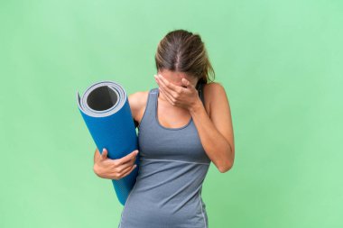 Güzel Uruguaylı genç spor kadın yoga derslerine gidiyor. Elinde yorgun ve hasta bir ifadeyle izole edilmiş bir arka planda minder tutuyor.