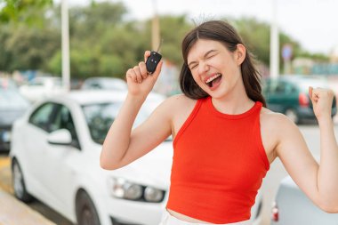 Açık havada elinde araba anahtarlarıyla genç ve güzel bir kadın zaferi kutluyor.