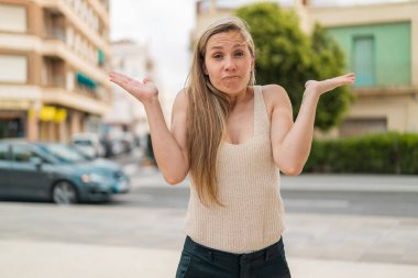 Açık havada genç sarışın bir kadın ellerini kaldırırken şüphe duyuyor.