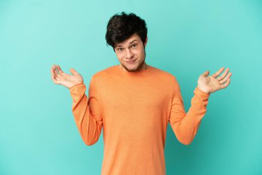 Genç Rus adam mavi arka planda izole edilmiş, ellerini kaldırırken şüpheye düşmüş.