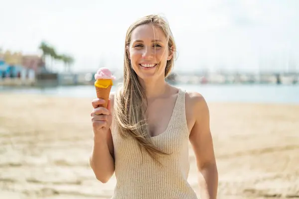 Young blonde woman with a cornet ice cream at outdoors with happy expression