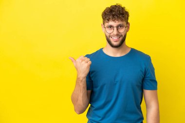 Sarı arka planda izole edilmiş yakışıklı beyaz adam bir ürün sunmak için yan tarafı işaret ediyor.