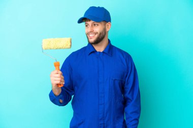 Kafkasyalı ressam mavi arka planda izole edilmiş. Kolları kalçasında ve gülümsüyor.