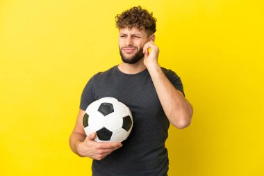 Yakışıklı genç futbolcu sarı arka planda izole edilmiş hayal kırıklığına uğramış ve kulaklarını kapatmış.