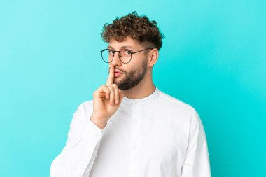 Mavi arka planda gözlüklü ve sessiz hareketler yapan yakışıklı beyaz bir adam.