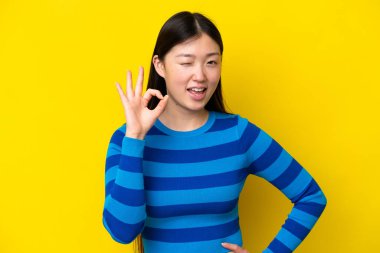 Young Chinese woman isolated on yellow background showing ok sign with fingers