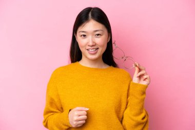 Genç Çinli bir kadın pembe arka planda izole edilmiş, mutlu bir ifadeyle gözlüklü.