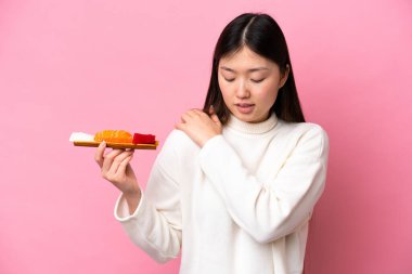Sashimi 'yi pembe arka planda tutan genç Çinli kadın çabaladığı için omuz ağrısından muzdarip.