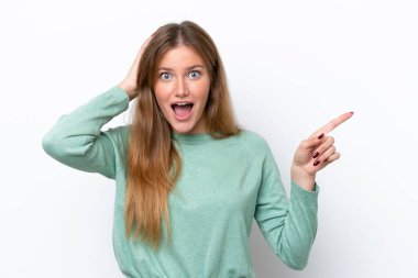 Beyaz arka planda izole edilmiş genç beyaz kadın şaşırmış ve işaret ediyor.