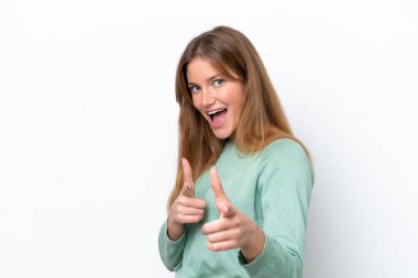 Beyaz arka planda izole edilmiş genç beyaz kadın ön tarafı işaret ediyor ve gülümsüyor.