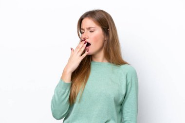 Beyaz arka planda izole edilmiş genç beyaz bir kadın esniyor ve geniş bir ağzı eliyle kapatıyor.