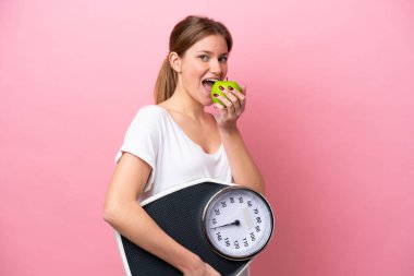 Pembe arka planda, tartı makinesi ve elmasıyla izole edilmiş beyaz bir kadın.