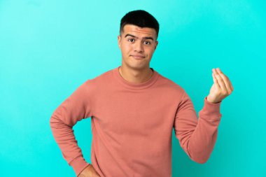 Soyutlanmış mavi arka planda genç yakışıklı bir adam İtalyan jesti yapıyor.