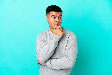 Soyutlanmış mavi arka planda genç yakışıklı bir adam yukarı bakarken bir fikir düşünüyor.