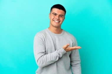 Soyutlanmış mavi arka planda genç yakışıklı bir adam gülümseyerek bir fikir sunuyor.