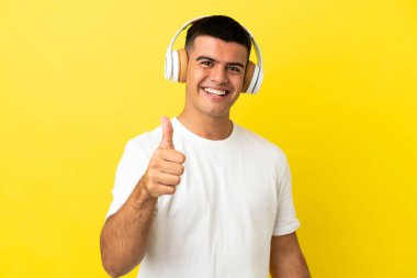 Soyutlanmış sarı arka planda genç yakışıklı adam müzik dinliyor ve başparmağını kaldırıyor.
