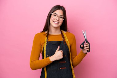 Pembe arka planda izole edilmiş genç Brezilyalı terzi kadın baş parmak hareketi yapıyor.
