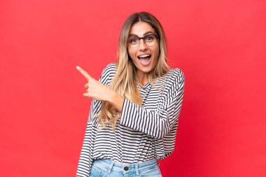 Genç Uruguaylı kadın kırmızı arka planda izole edilmiş. Şaşırmış ve işaret ediyor.