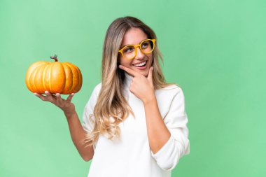 Genç Uruguaylı kadın izole edilmiş bir arka planda balkabağı tutarken bir fikir üretiyor ve ona bakıyor.