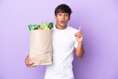 Elinde mor arka planda izole edilmiş bir alışveriş poşeti tutan genç adam çözümü bulmak için parmağını kaldırıyor.