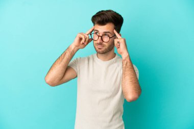 Kafkasyalı yakışıklı adam mavi arka planda izole edilmiş. Şüpheleri ve düşünceleri var.