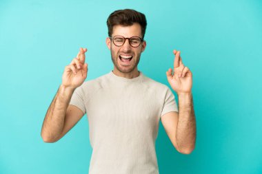 Beyaz tenli yakışıklı adam mavi arka planda izole edilmiş ve şans diliyor.