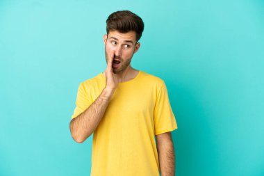 Beyaz tenli yakışıklı adam mavi arka planda izole edilmiş. Yan tarafa bakarken sürpriz bir jest yapıyor.