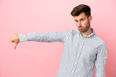 Pembe arka planda izole edilmiş beyaz, yakışıklı genç adam, olumsuz bir ifadeyle baş parmağını aşağı gösteriyor.