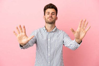 Pembe arka planda izole edilmiş beyaz tenli yakışıklı adam parmaklarıyla ona kadar sayıyor.