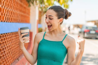 Genç ve güzel bir kadın açık havada kahvesini yudumluyor ve zaferi kutluyor.