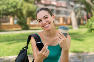 Dışarıda cep telefonu kullanan ve elinde kahve tutan genç ve güzel bir kadın.