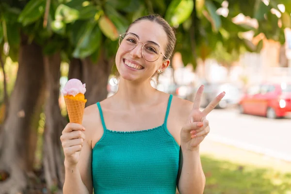 Young pretty woman with a cornet ice cream at outdoors smiling and showing victory sign