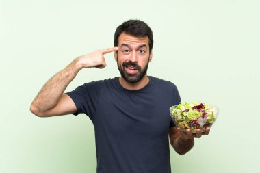 Yeşil duvarın üstünde salatalı yakışıklı bir adam deliliğin jestini yapıyor. Parmağını başına koyuyor.