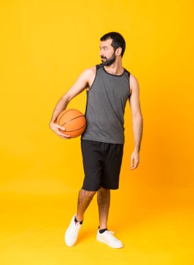 İzole edilmiş sarı arka planda basketbol oynayan bir adamın tam boy çekimi.