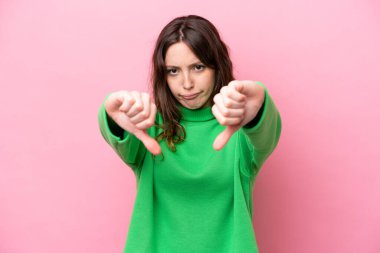 Pembe arka planda izole edilmiş beyaz bir kadın baş parmağını iki eliyle aşağı gösteriyor.