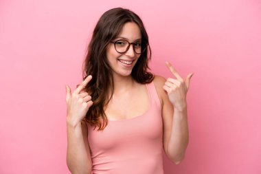 Pembe arka planda izole edilmiş beyaz bir kadın baş parmak hareketi yapıyor.