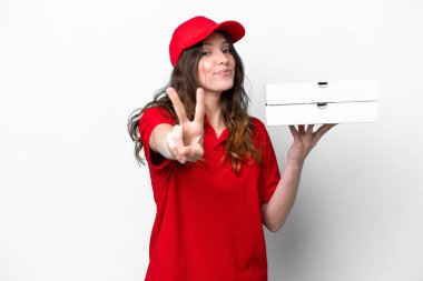 Pizza dağıtan kadın iş üniformalı beyaz arka planda izole edilmiş pizza kutuları alıyor gülümsüyor ve zafer işareti gösteriyor.